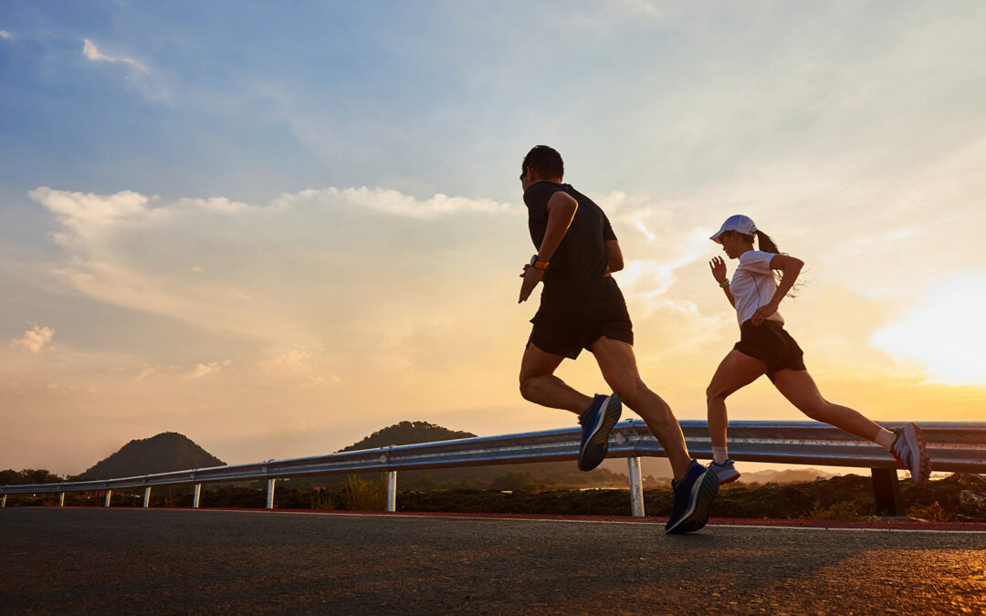A man and a woman running on a road next to each other against a sunset backdrop.